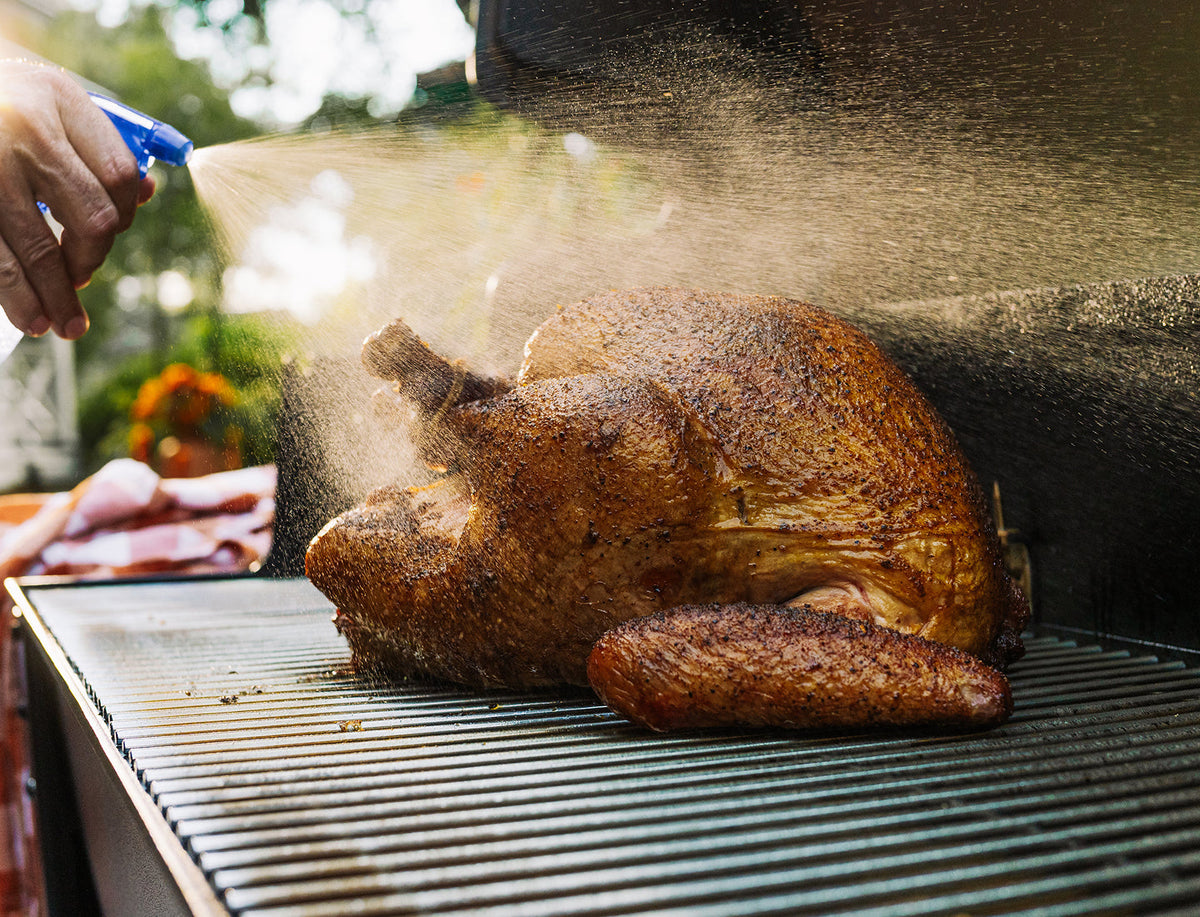 Roasted turkey being seasoned on a grill with a blurred outdoor background